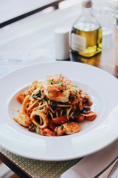 Octopus vs. Calamari – What’s the Difference? 4 A plate of calamari, shrimp, and pasta in red sauce served on a white plate beside a bottle of out-of-focus olive oil and a white salt shaker.