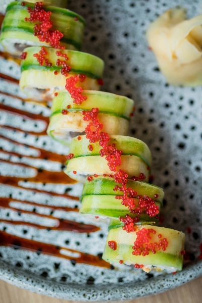 A colorful sushi roll wrapped in avocado and topped with orange roe on a plate drizzled with eel sauce.