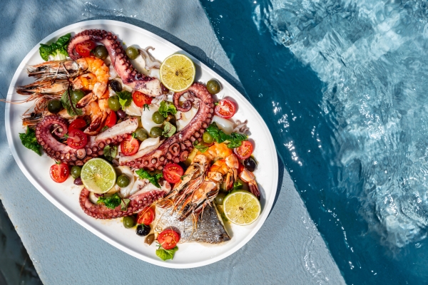Octopus vs. Calamari – What’s the Difference? 1 A white oval plate with octopus, fish, tomatoes, citrus wedges, and greens rests beside clear blue pool water.