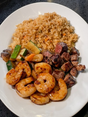 An overhead shot of a plate filled with fried rice, vegetables, chicken, steak, and shrimp.